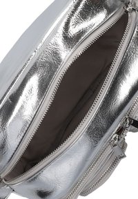 Zilveren metallic rugzak met een gladde, glanzende buitenkant, dubbele ritssluitingen en een met stof beklede binnenkant in donkerbruin.