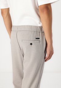 Hellgraue Hose aus strukturiertem Stoff, mit elastischem Bund und einer einzelnen Gesäßtasche mit einem schwarzen Knopf und Labeldetail.