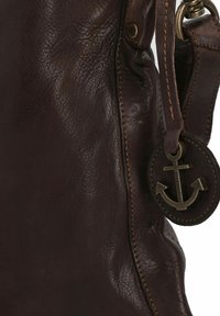 Borsa in pelle marrone scuro con cuciture visibili e un'etichetta rotonda in pelle attaccata, con un emblema di ancoraggio in bronzo.
