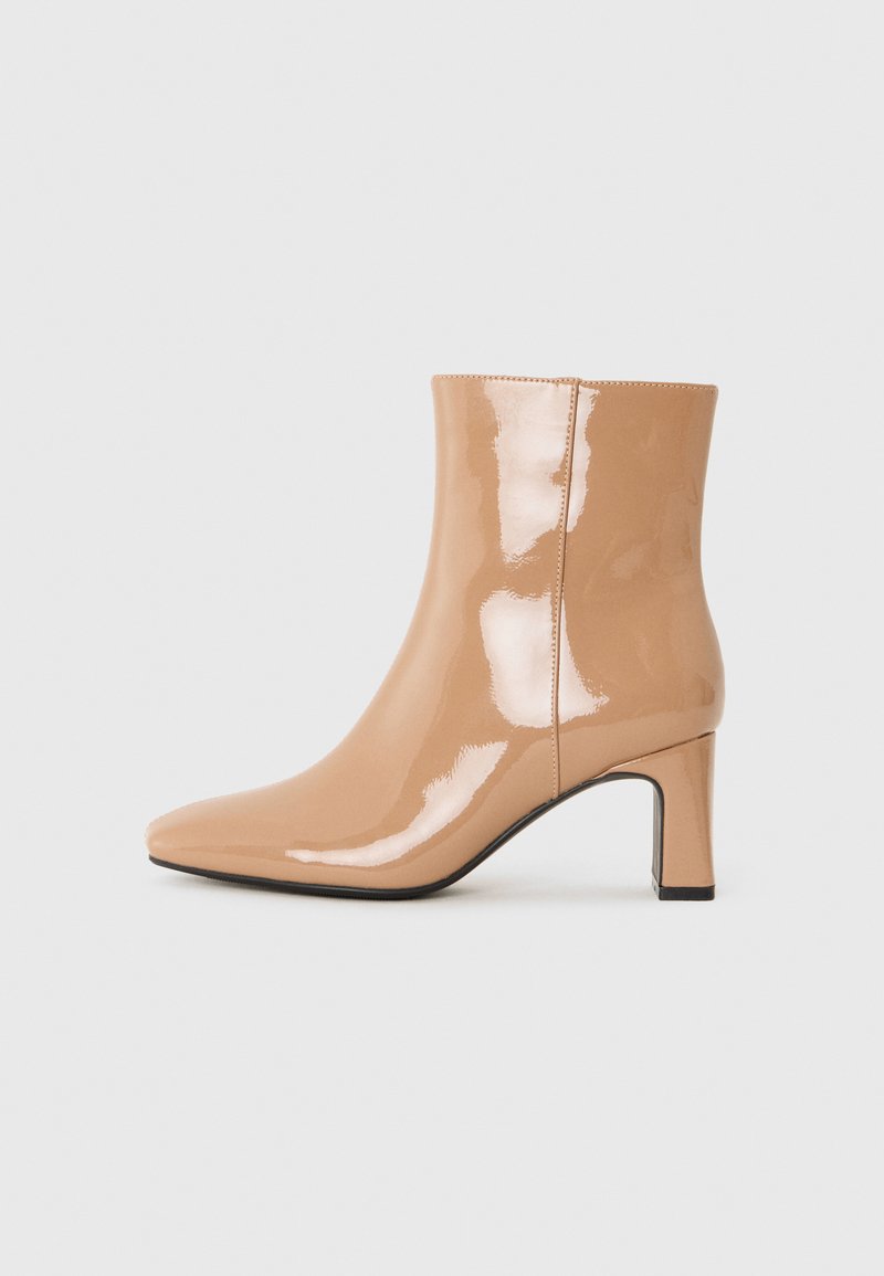 Nude lakované kotníkové boty s špičatou špičkou, lesklým povrchem a středně vysokým blokovým podpatkem. Hladký texture a elegantní silueta.