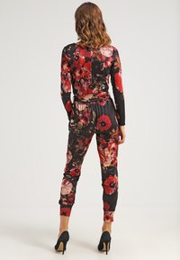 Jumpsuit floreale nero, con motivi rossi e rosa, maniche lunghe, vita elasticizzata e polsini a gamba affusolata. Abbinato a tacchi neri.