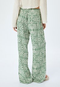 Groene, gestreepte wijdlopende broek gemaakt van lichte stof met een wit geometrisch ontwerp. Elastische tailleband, zijzakken en een ontspannen pasvorm.
