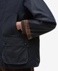 Casaco impermeável azul com punhos xadrez castanhos, apresentando bolsos laterais e fechos de pressão. Feito de tecido suave com um corte descontraído.