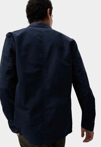 Granatowa bawełniana koszula z kołnierzykiem, długimi rękawami i zapięciem na guziki przy mankietach. Posiada gładką strukturę oraz detal w postaci szwu z tyłu.