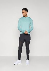 Lichtblauwe sporttop met lange mouwen en een kwartrits, zwarte korte broek, zwarte legging, afgewerkt met witte sportschoenen.