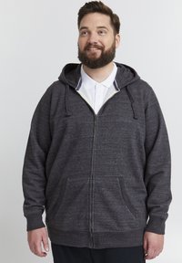 Grå zip-up hettegenser laget av teksturert stoff, med glidelås foran, snorer på hetten og store sidelommer.