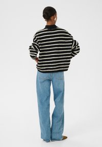 Zwarte en crèmekleurige gestreepte trui met een relaxte fit, gecombineerd met hooggeknoopte, lichtblauwe jeans. Zachte gebreide textuur en oversized mouwen.
