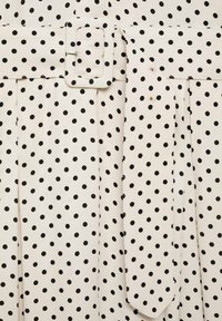 Tessuto bianco con pois neri, dotato di una cintura ampia con fibbia quadrata, pieghe laterali e superficie liscia.
