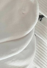 Weißer Stoff mit einer glatten, leicht strukturierten Oberfläche; mehrere abgerundete Schichten sind sichtbar, mit feinen Nähten und subtiler Glanz.