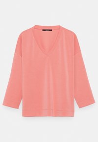 Chemise rose corail à manches longues, col en V et coupe ample, présentée sur un fond clair uni.