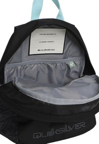 Interior de mochila negra Quiksilver con forro gris, que cuenta con una etiqueta para información del propietario y un bolsillo de malla para organización.