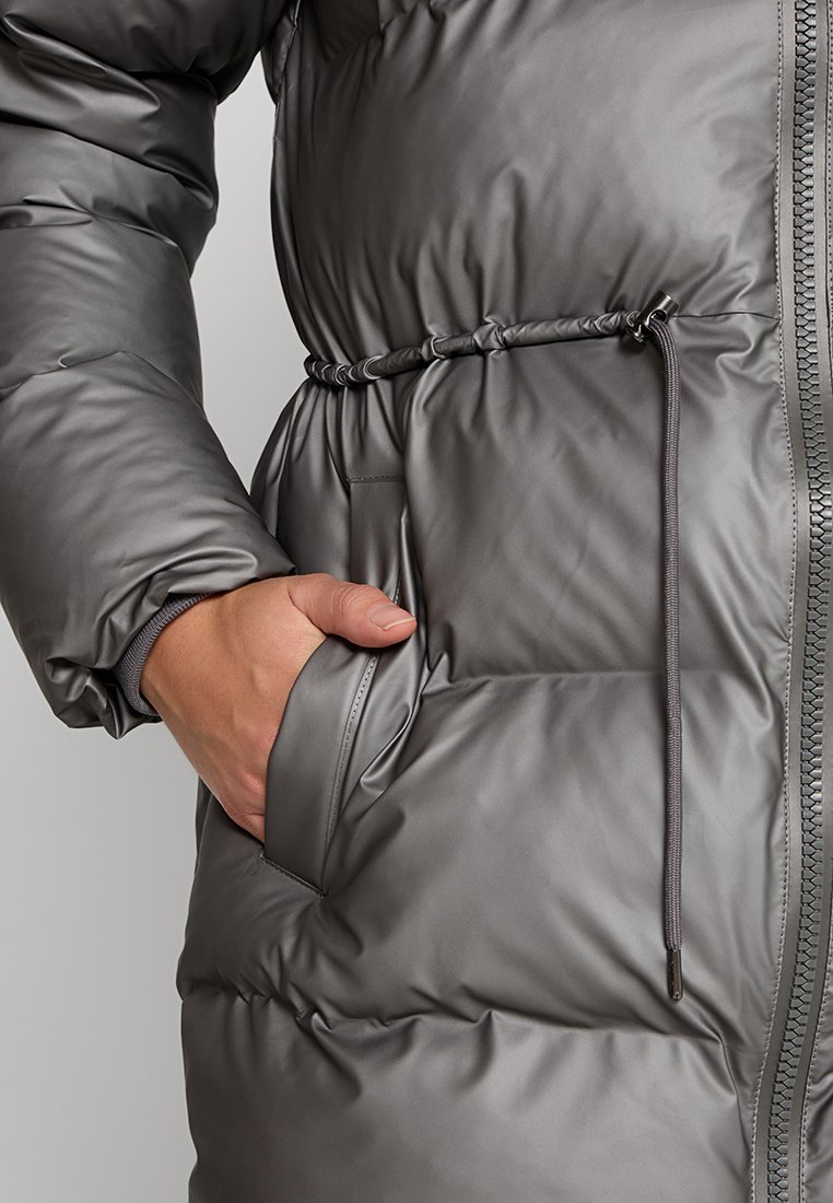 Manteau rembourré gris avec taille cintrée, doté d'une poche latérale, d'une texture lisse et d'un détail zip sur le devant.
