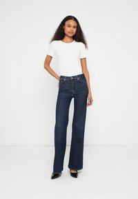 High-waisted dark blue denim jeans with wide legs, paired with a fitted white T-shirt. Smooth fabric and classic five-pocket design.
