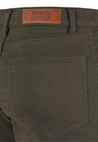 Tissu vert olive d'un pantalon avec une étiquette en cuir marron et une poche arrière unique avec des détails de couture renforcée.