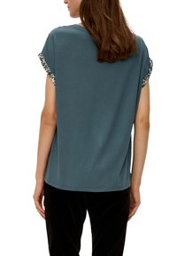Türkisfarbener Kurzarmshirt mit dekorativen Musterakzenten am Ärmel, lockerer Passform, weichem Material und schlichter Rückseite.