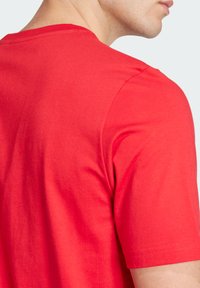 Rotes Baumwoll-T-Shirt mit Rundhalsausschnitt und kurzen Ärmeln, das eine glatte Textur und minimale Nähtdetails am Ausschnitt und Saum aufweist.