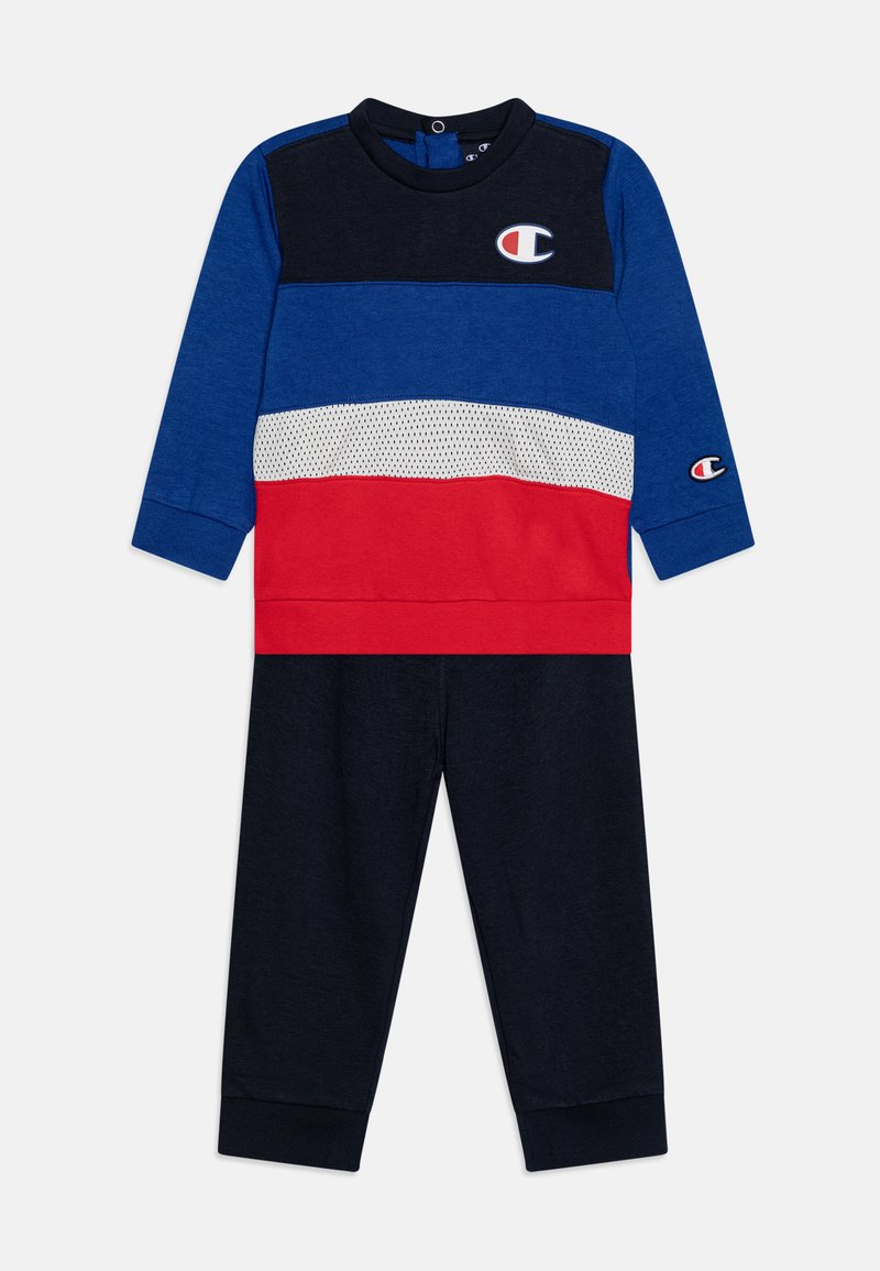 Tuta per bambini a maniche lunghe in blu, rosso e nero con logo, caratterizzata da inserti di colore, una striscia in rete e polsini elastici sui pantaloni.