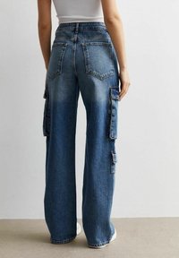 Jeans cargo de pierna ancha en denim azul claro, con dos bolsillos laterales y dos bolsillos traseros, que muestran una textura desgastada.