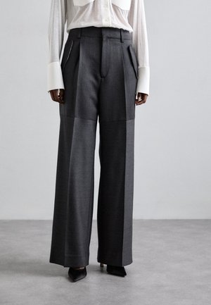 Højtaljede bukser med brede ben i mørkegrå stof. Har frontfolder og diskrete sidelommer, parret med spidse sorte hæle.