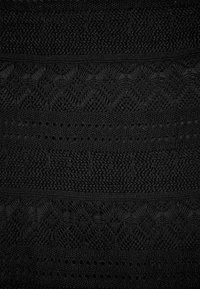Tessuto di pizzo nero con intricati motivi a forma di diamante e ritagli circolari, caratterizzato da un aspetto tessuto e diversi design di cucitura.