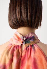 Ärmellose Bluse mit einem mehrfarbigen Batikmuster, die einen hohen Kragen und drei metallische Knöpfe auf der Rückseite besitzt. Leichtes, fließendes Material.