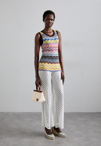 Débardeur en tricot à motif zigzag multicolore, pantalon large en crochet blanc, mini sac à main beige et chaussures de style espadrilles multicolores.