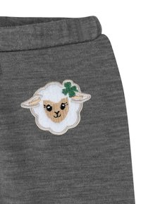 Grauer Stoff mit einer weichen Textur, der ein weißes, gesticktes Schafdesign zeigt, das von einem grünen Kleeblatt auf dem Kopf akzentuiert wird.