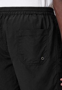 Pantalones cortos negros hechos de un tejido ligero con una cintura elástica. Cuenta con un bolsillo de parche con un detalle de ojal metálico.