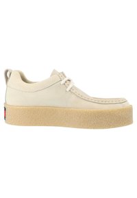 Scarpe in suede beige con punta tondeggiante, lacci bianchi e una suola piatta in tessuto marrone chiaro. Sul retro è presente un piccolo dettaglio con il logo.