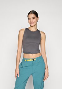 Grauer ärmelloser Crop-Top kombiniert mit türkisfarbenen Hosen, die einen gelben Gürtel besitzen. Der Stoff wirkt glatt und hat ein figurbetontes Design.