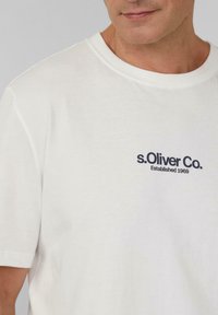 Witte katoenen T-shirt met korte mouwen en ronde hals, voorzien van een donkerblauw logo "s.Oliver Co." en "Established 1969" op de borst.