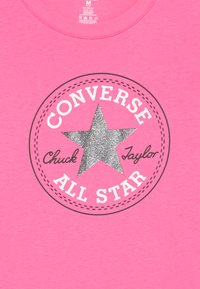 T-shirt en coton rose avec un motif circulaire comportant une étoile argentée pailletée, des contours noirs et le texte « CONVERSE ALL STAR ». 