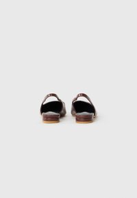 Pantofi slip-on din piele maro, cu spatele deschis, având un finisaj neted și o talpă plată. Interiorul este negru, cu detalii hardware minime.