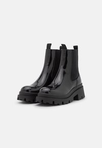 Las botas de tobillo de charol negro cuentan con una suela gruesa, paneles elásticos en los laterales y lengüetas para facilitar su uso. Diseño elegante y moderno.