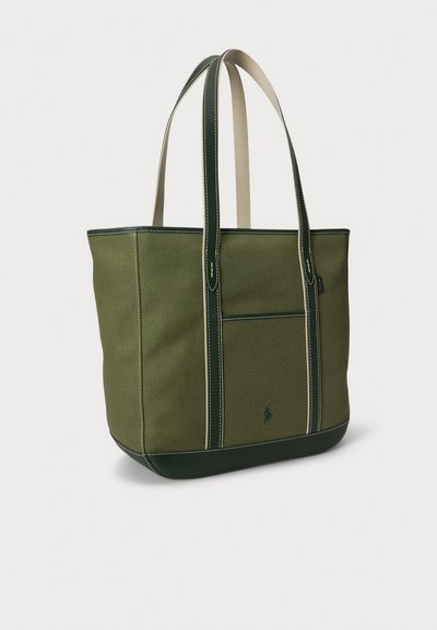 Τσάντα ώμου από καμβά σε ελιά με σκούρες πράσινες λεπτομέρειες, χειρολαβές σε κρεμ απόχρωση και αντιθετικές ραφές. Διαθέτει μπροστινή τσέπη και λογότυπο στο πλάι.