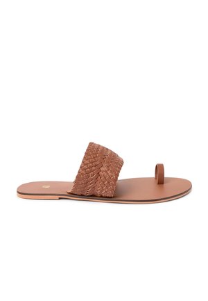 Sandale plate en cuir marron avec une large lanière tissée sur le pied et une boucle pour orteil unique sur fond blanc.
