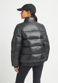 Giacca a vento nera con colletto alto, design trapuntato e polsini elasticizzati. Realizzata in materiale lucido, presenta una vita aderente e accento con logo.