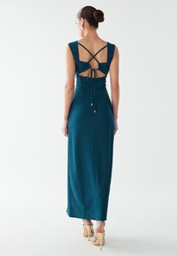 Blågrön maxiklänning med ränder, tajt överdel och öppen rygg med korslagda band och detalj med knytning. Mjukt, lätt tyg.