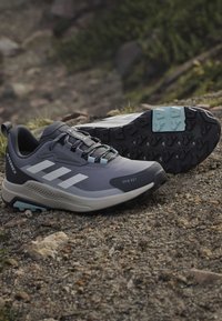 Chaussures de randonnée Adidas Terrex grises et noires avec des accents bleu clair reposant sur un sol rocheux en plein air.