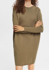 Robe en tricot vert olive avec de longues manches, des poignets côtelés et une coupe ample, présentant un col rond et une texture lisse.