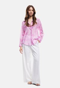 Rosa, durchsichtige Bluse mit Knopfverschluss und floralem Muster, kombiniert mit weiten weißen Hosen und minimalistischen Sandalen. Glatte Textur und taillierte Passform.