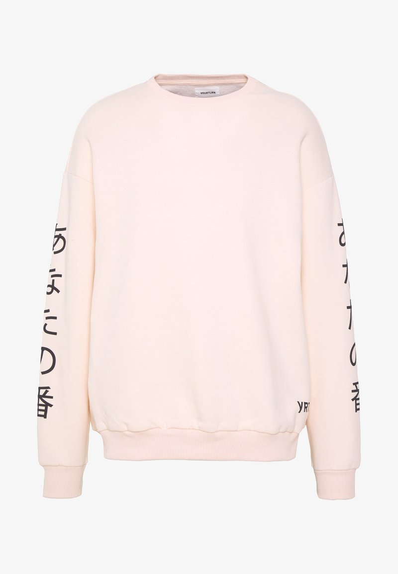 Sweatshirt rose clair à manches longues, avec poignets et ourlet côtelés, comportant un texte noir le long des manches et un logo près du bas.