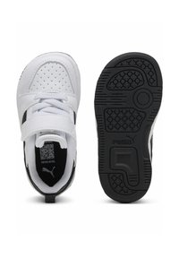 Baskets blanches et noires avec une tige en synthétique, un design perforé, une sangle Velcro et une semelle en caoutchouc noir texturé avec des motifs de grip.