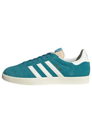 Baskets Adidas Gazelle en daim bleu sarcelle avec des bandes blanches, languette blanche au talon et semelle texturée écrue, vue de côté sur fond blanc.