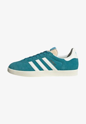 Türkisfarbener Adidas Gazelle Sneaker aus Veloursleder mit weißen Streifen, weißer Fersenlasche und einer cremefarben texturierten Sohle, Seitenansicht vor weißem Hintergrund.