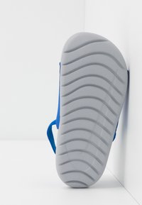 Sandale bleue avec une semelle en caoutchouc texturé. Présente une forme incurvée, des sangles bleues douces et une semelle grise flexible et striée pour une meilleure adhérence.
