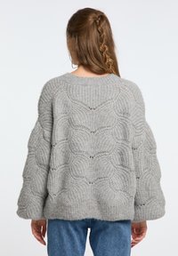 Tömött szürke kötött pulóver, melynek hullám mintázata van, kerek nyakkivágása és oversized ujjai. Az anyag lágy és bolyhos.