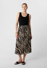 Schwarzes geripptes Tanktop kombiniert mit einem langen, fließenden Rock mit beigen und schwarzen Tigerstreifenmuster; getragen mit schwarzen Sandalen.