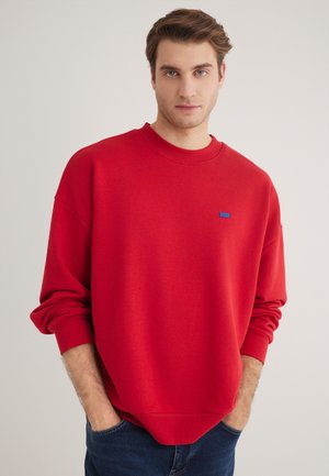 Red sweatshirt with a crew neck and long sleeves, featuring a small blue logo detail on the chest. Soft fabric and relaxed fit.