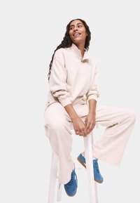 Crème kleurige sweatshirt van een katoenmix met een kwart rits en een borstzak, gecombineerd met bijpassende wijde broek. Blauwe sneakers.